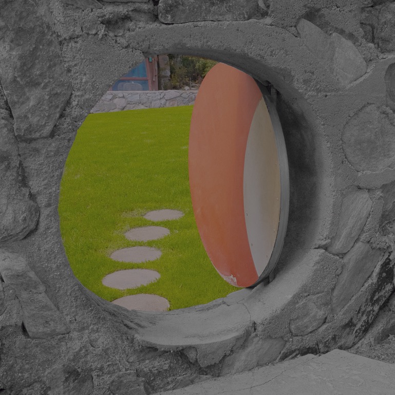 Circular portal in a stone wall at Taliesin West, framing a green lawn and a red disc in selective color